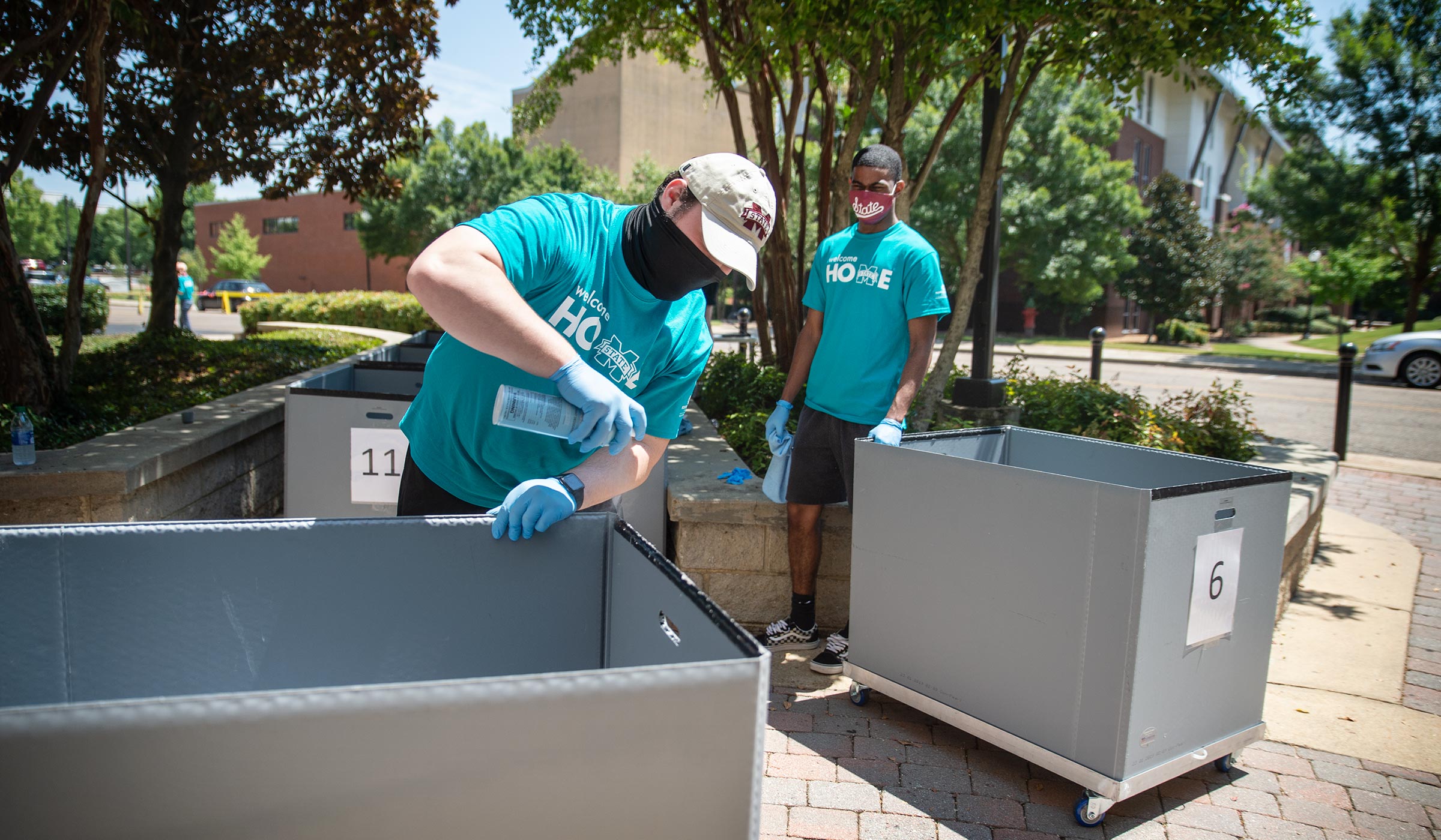 Masked MVNU2MSU Volunteers spray down the wheelie carts between students moving in to Hathorn Hall.