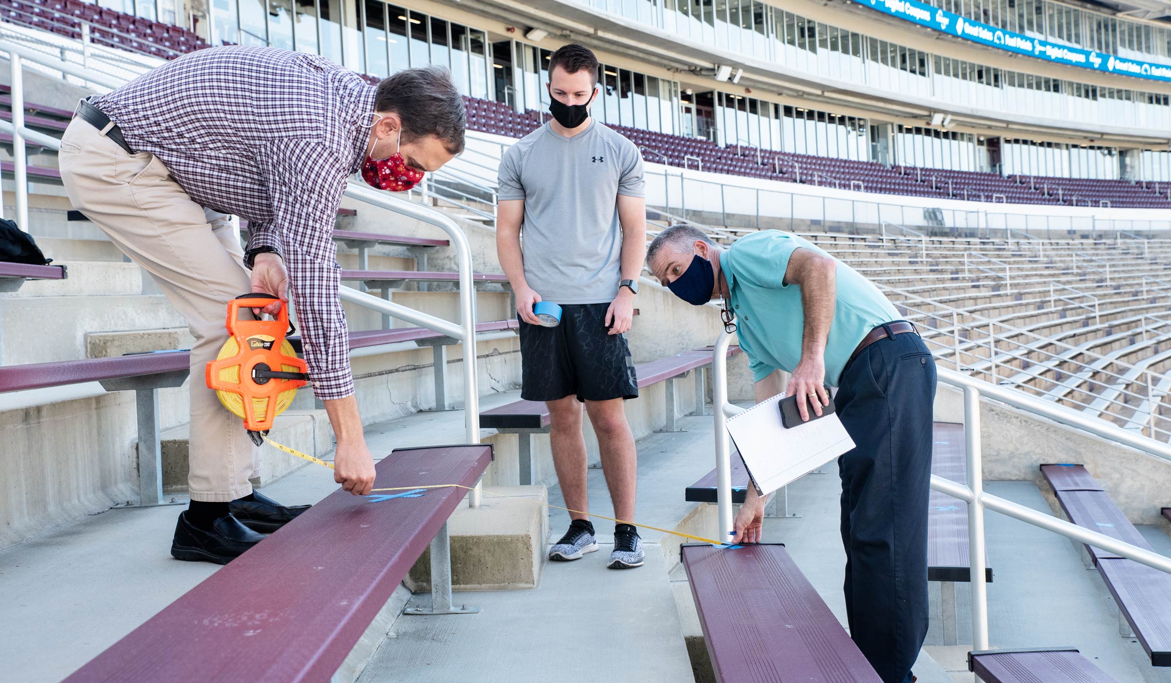 With the sweep of Davis Wade Stadium behind them, Band Directors use painters tape to mark socially-distanced seats for band.