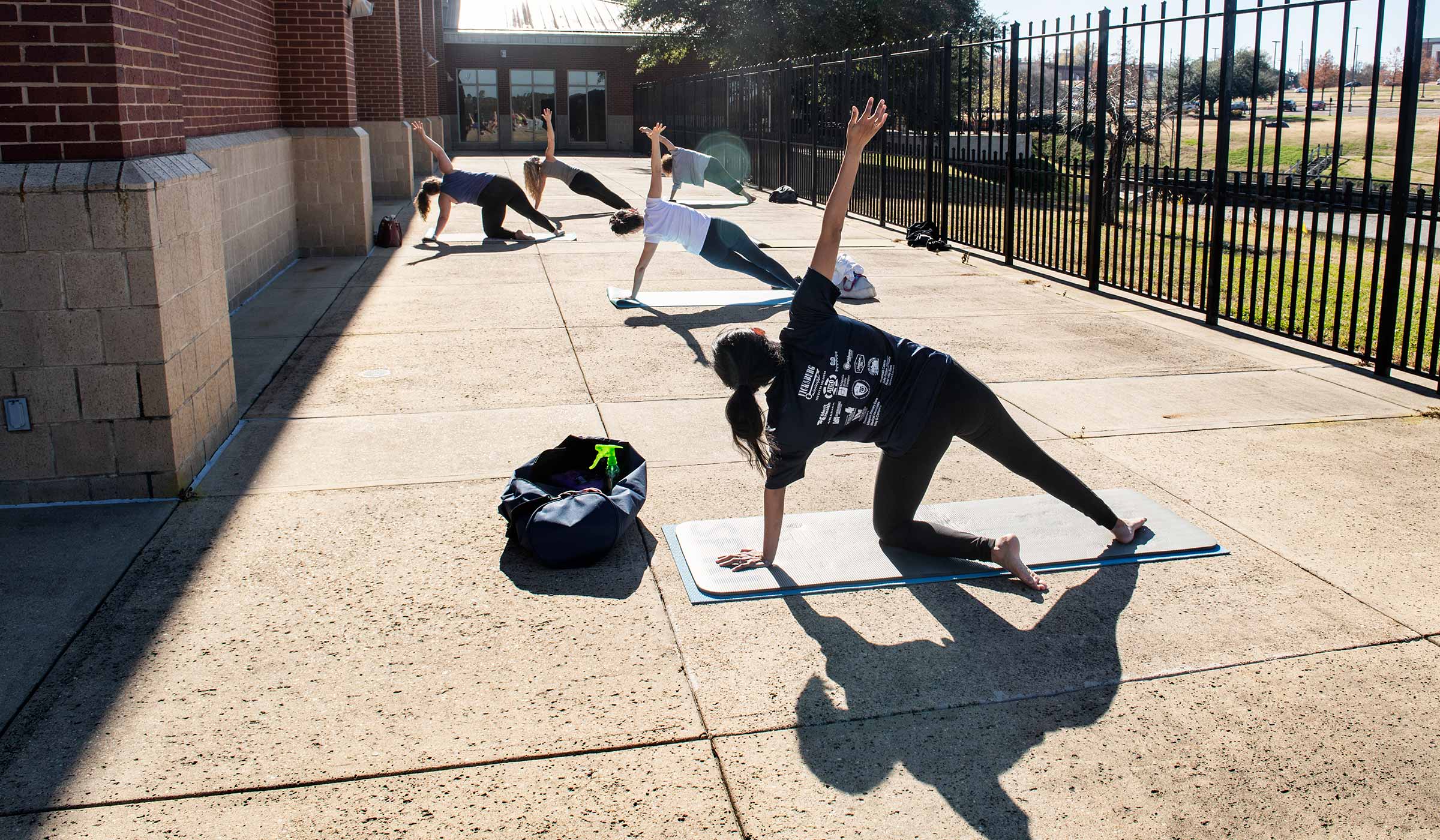 Five yoga class participants face the sun during class outside on the Sanderson patio.