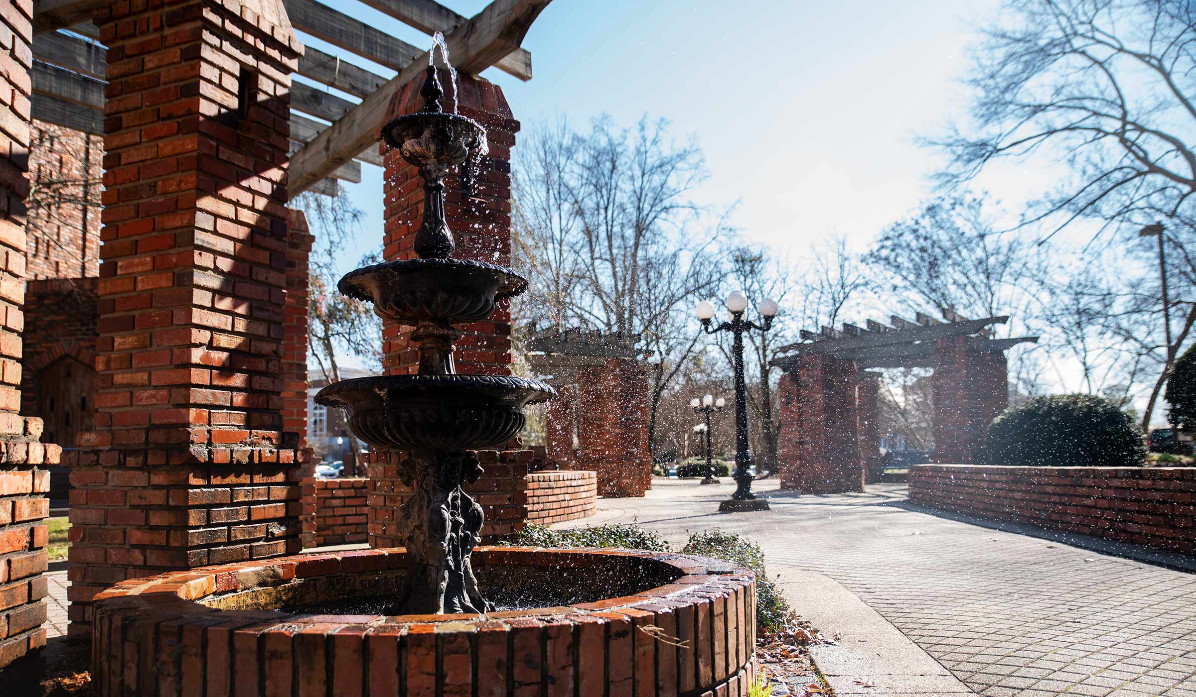 Metal water fountain with water trickling over edges to brick base