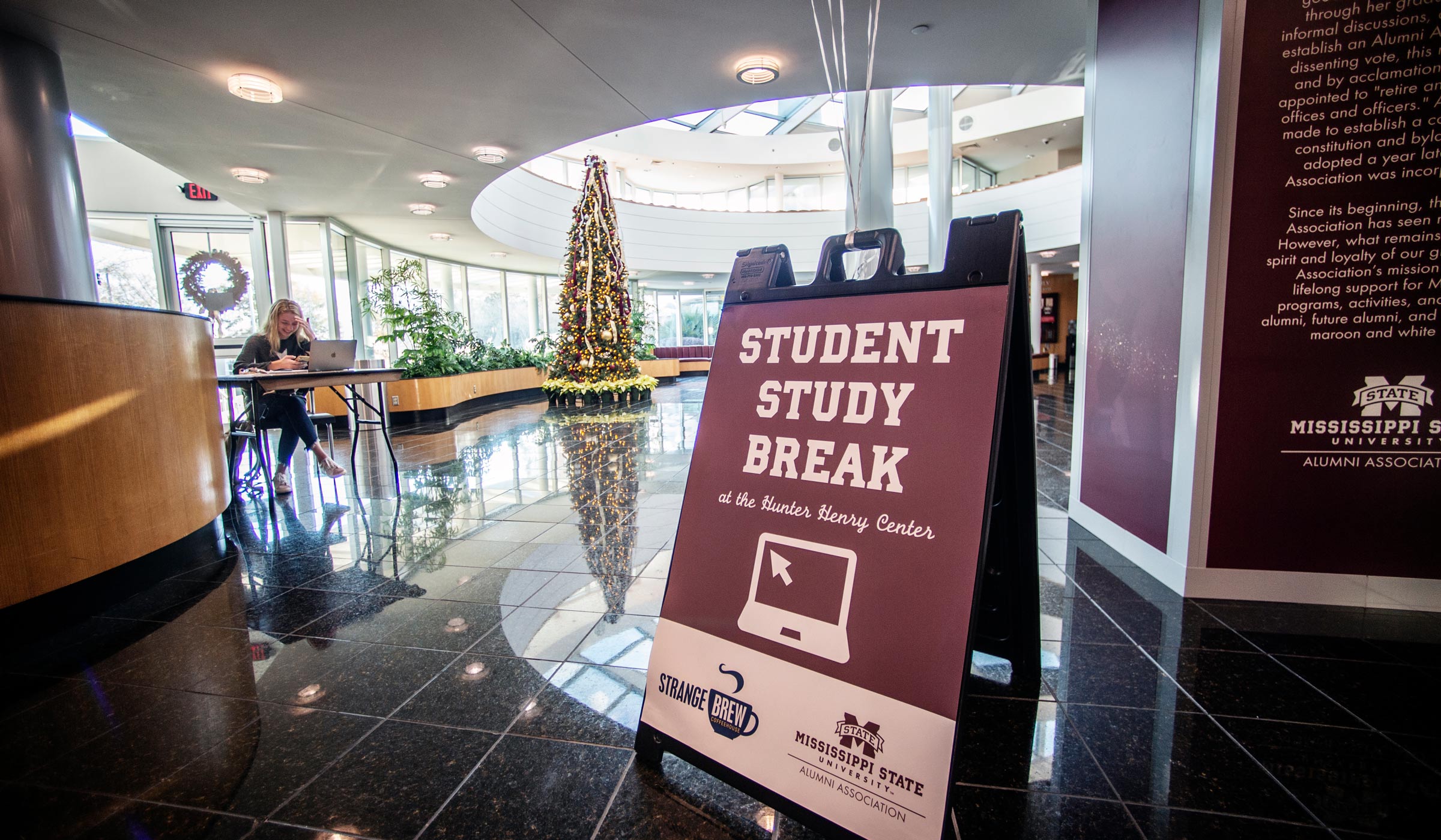 A sign reading &quot;Student Study Break&quot; stands in the foreground, with the Hunter Center Atrium Christmas tree and a studying student beyond.