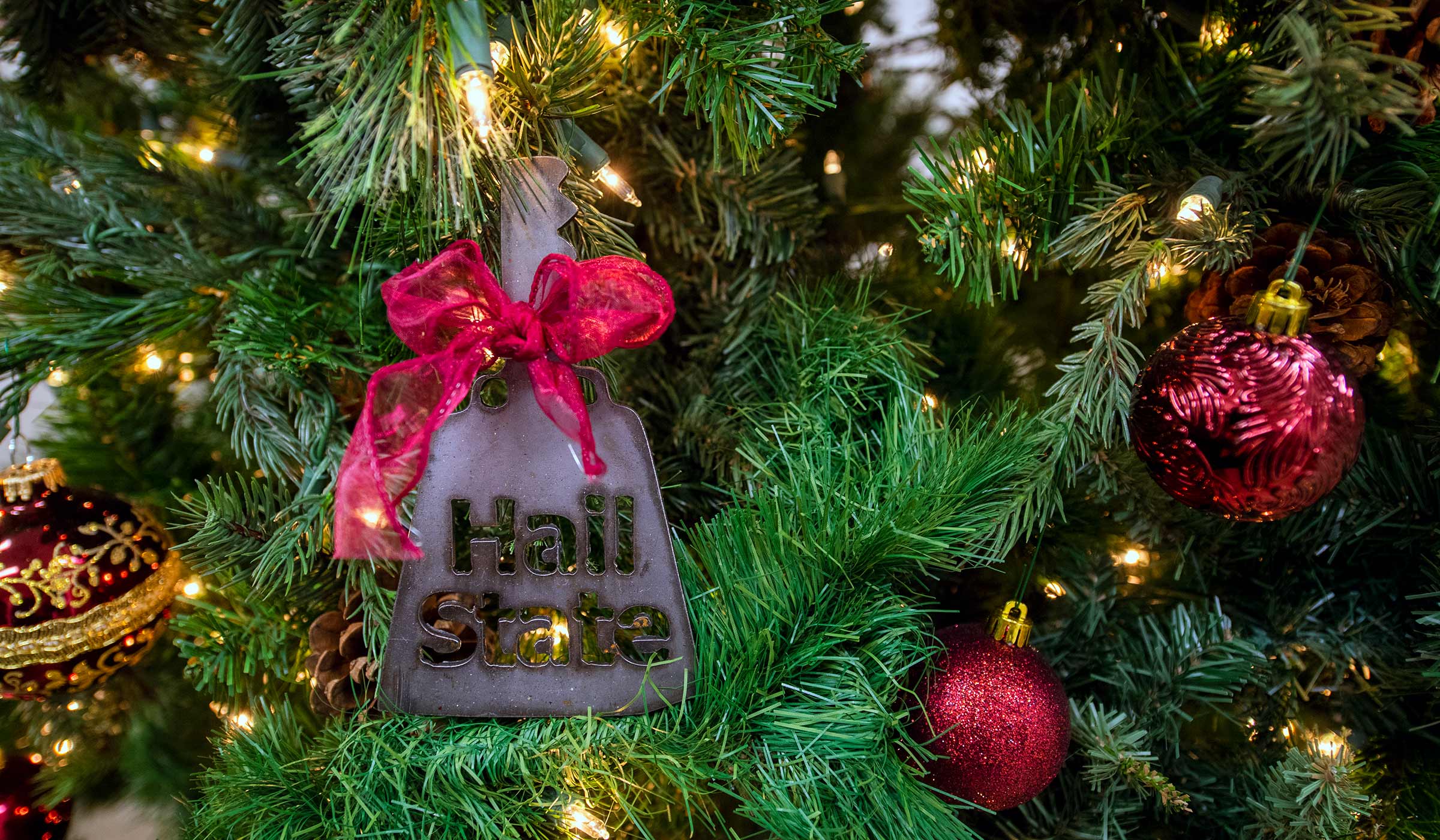 Sheet metal cowbell ornament with hail state on it with a maroon ribbon on Christmas tree