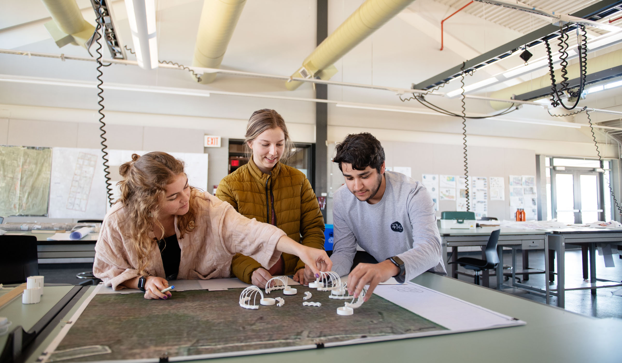 Three students work on rearranging model garden components in the Landscape Architecture studio.