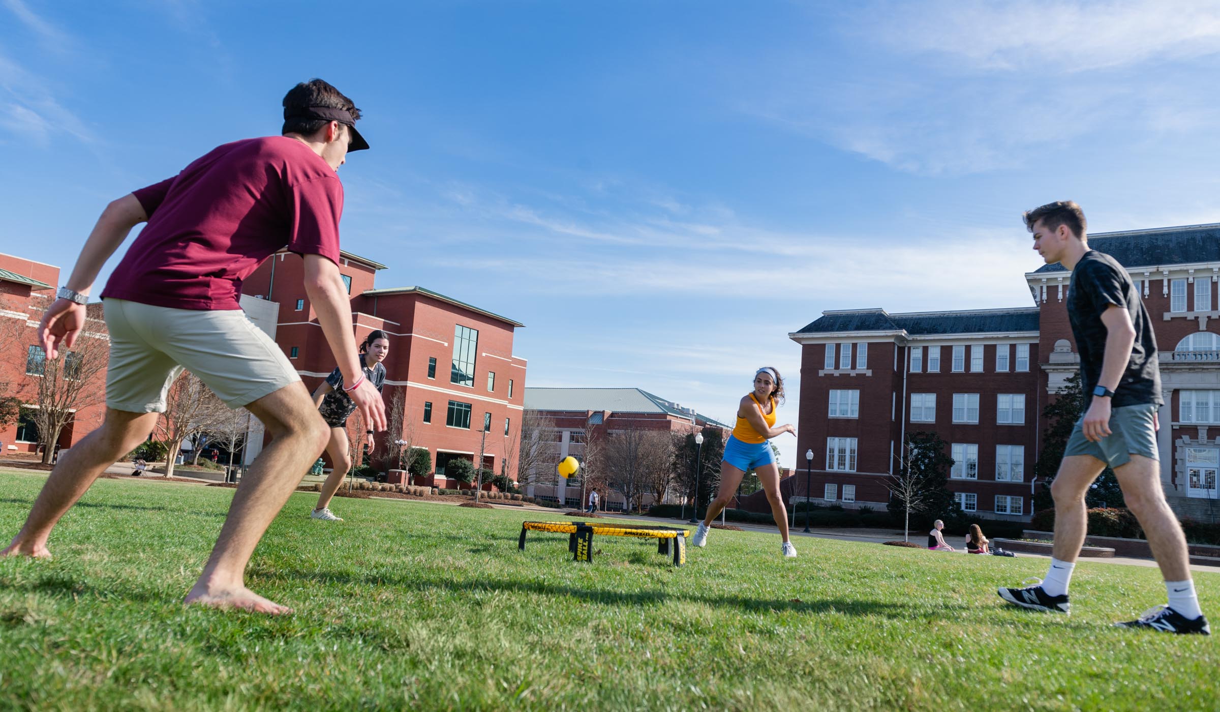 Four students are captured mid game while playing Spike Ball on the green grass near Mitchell Memorial Library and Swalm Hall.