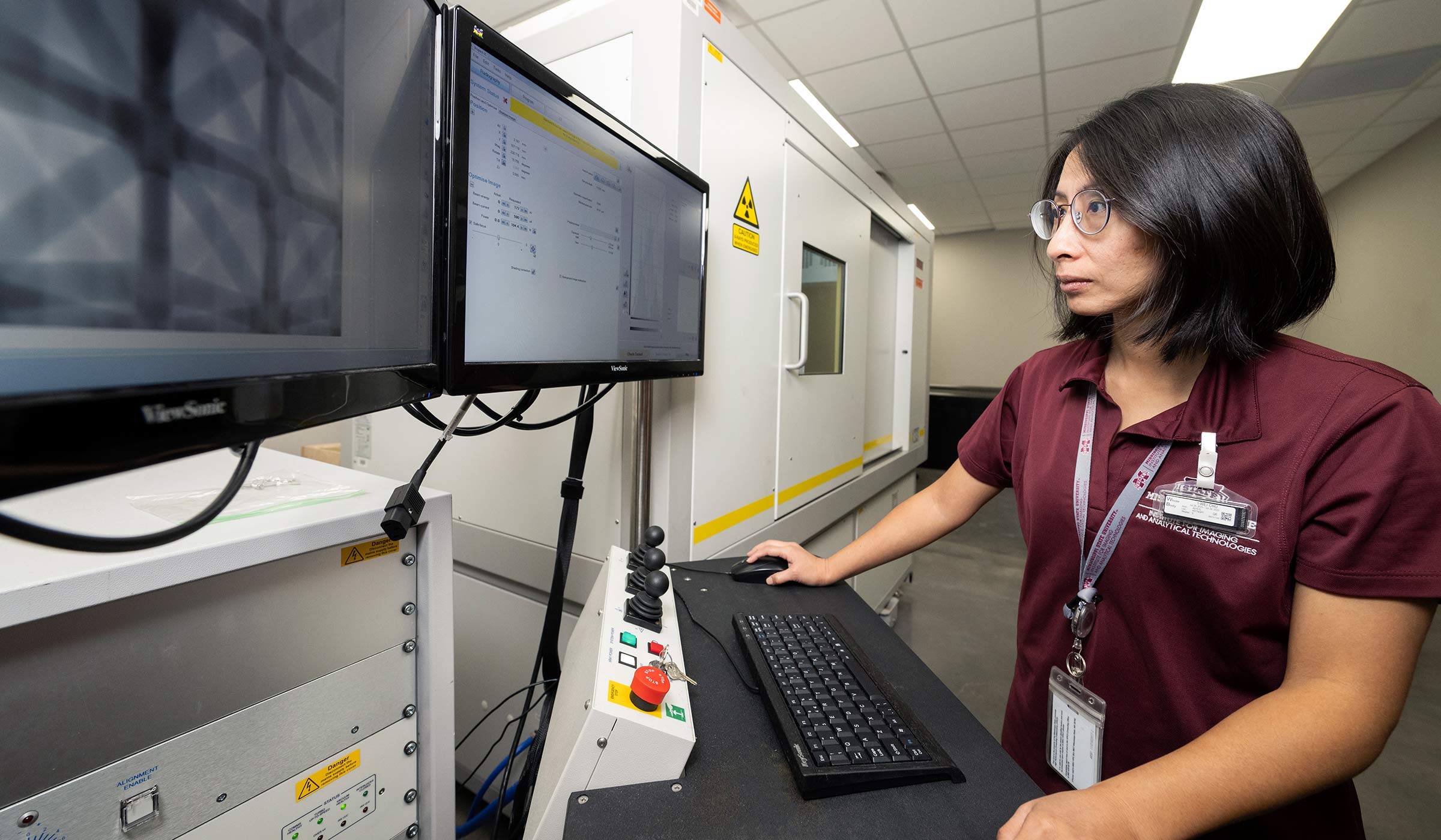 Woman at control panel with two screens with x-ray in background