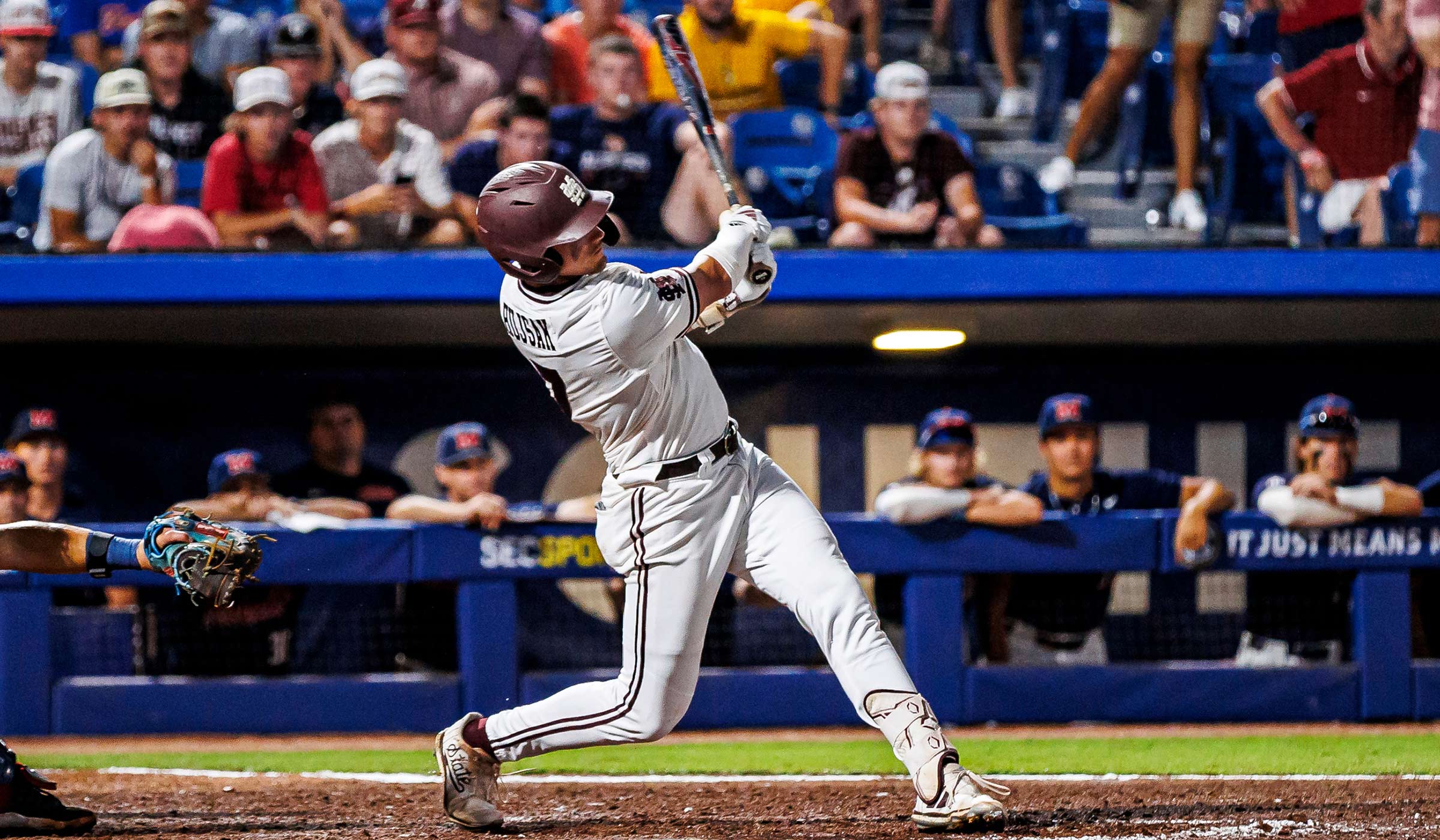 Baseball player in all white with maroon helmet swinging bat