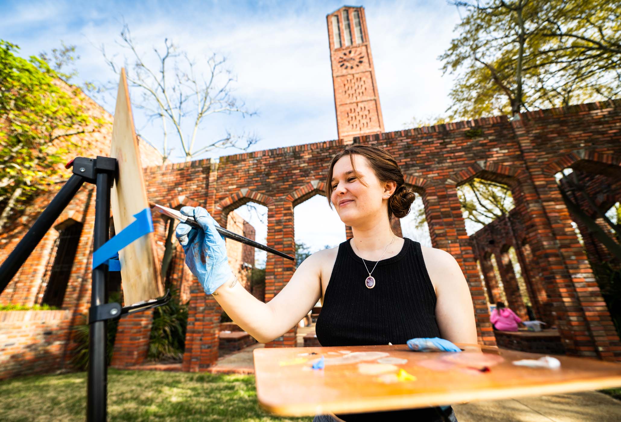 Sarah Perkins, a junior art student from insert hometown, and her classmates find inspiration at the Chapel of Memories, reinterpreting its angles with oil paint for their Painting Survey course. The pleasant springtime weather adds to the creative atmosphere, providing the perfect environment for the class's artistic exploration.