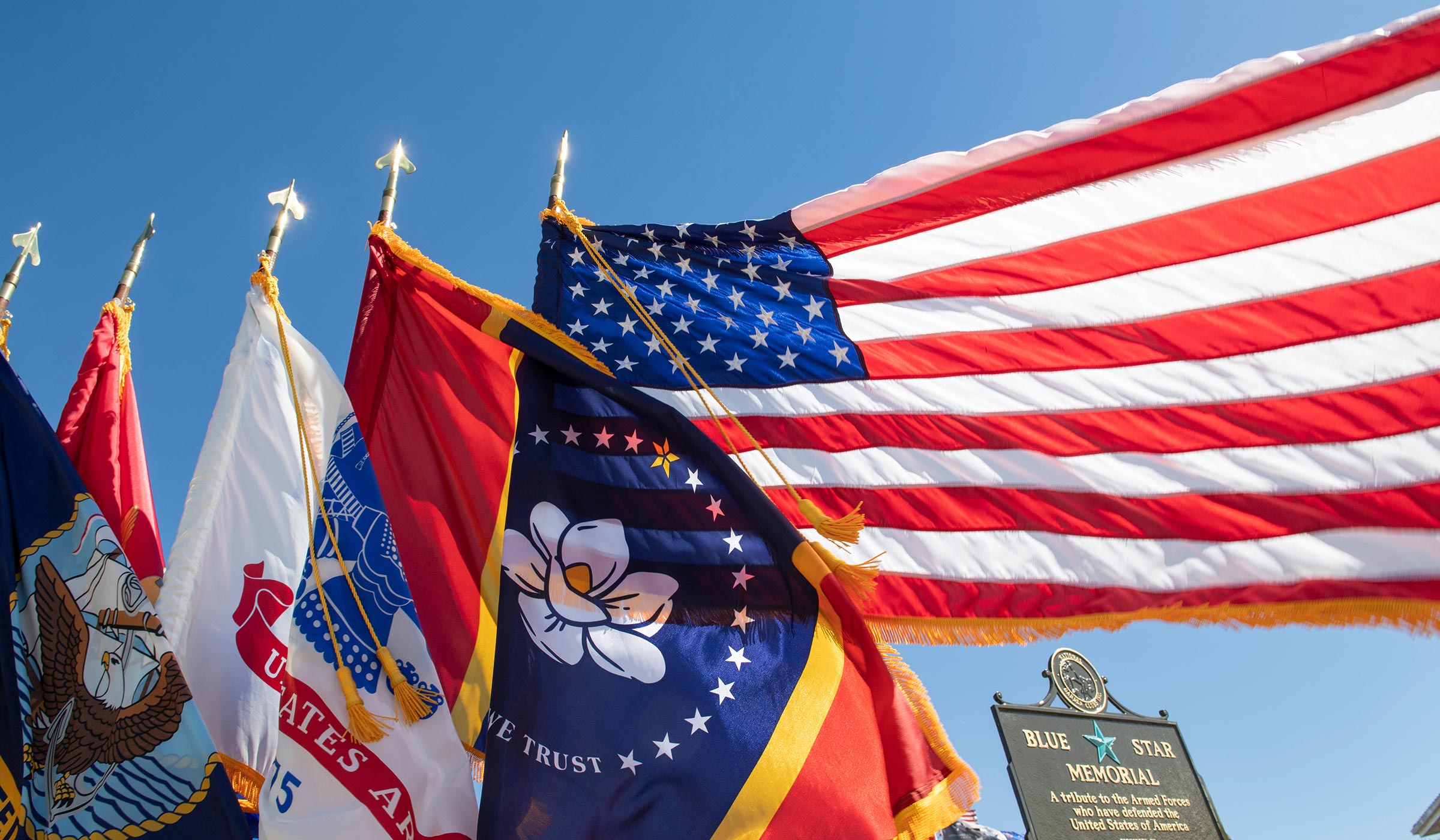 American flag and Mississippi state flag with military flags billowing in wind