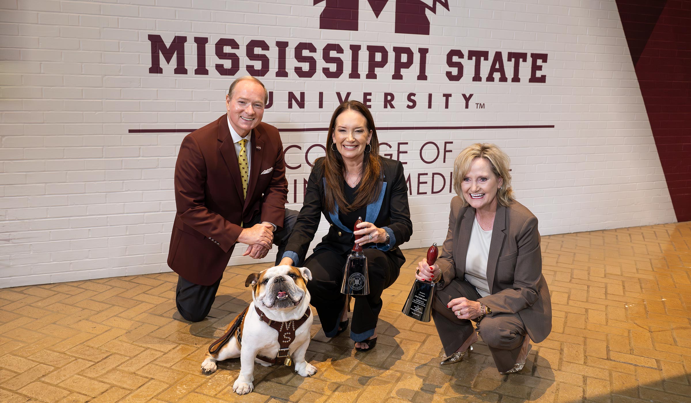 Three people - two holding chrome cowbells - posed with bulldog
