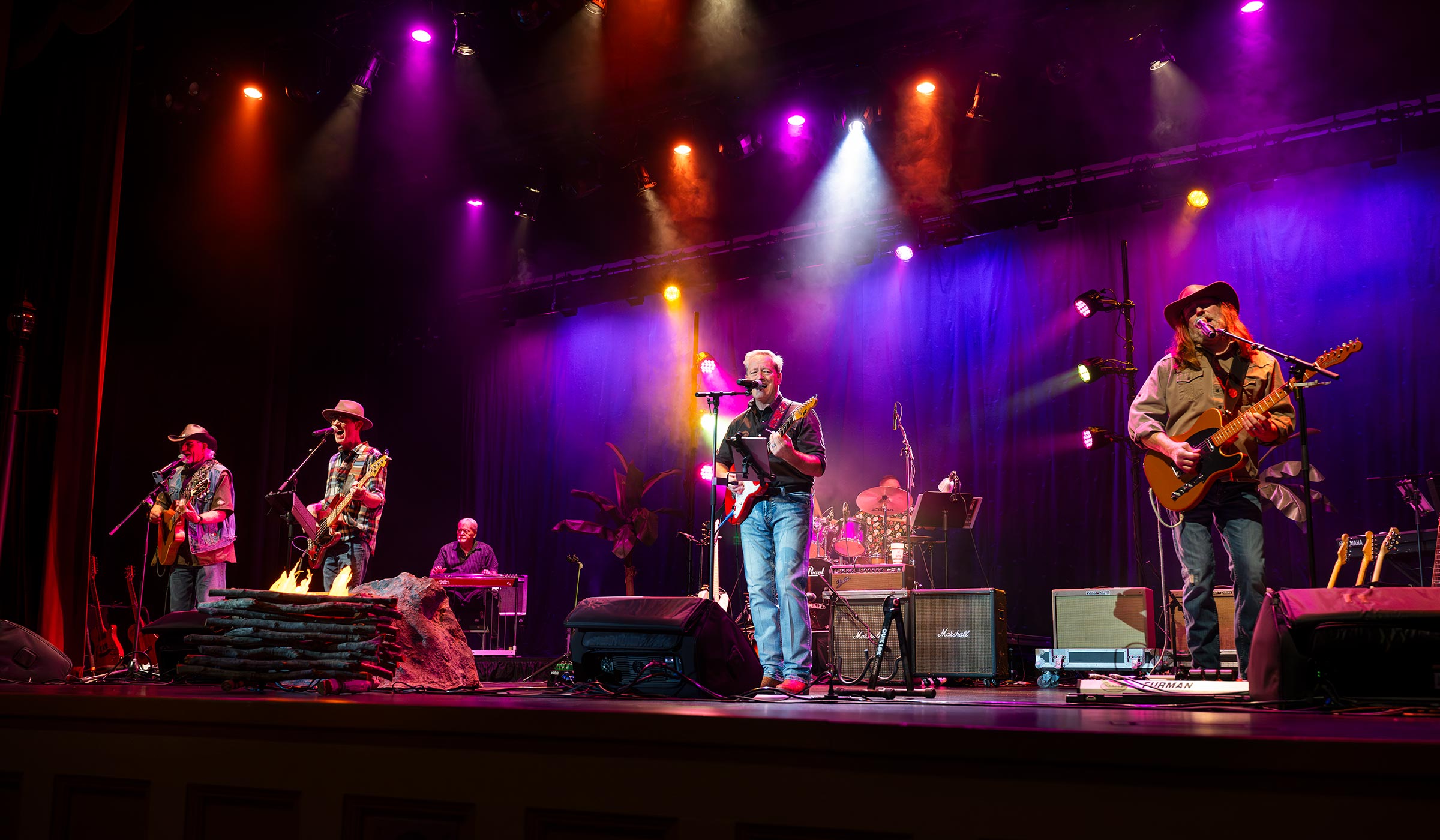 Rock band with guitars performing on stage with purple, pink, and orange stage lights