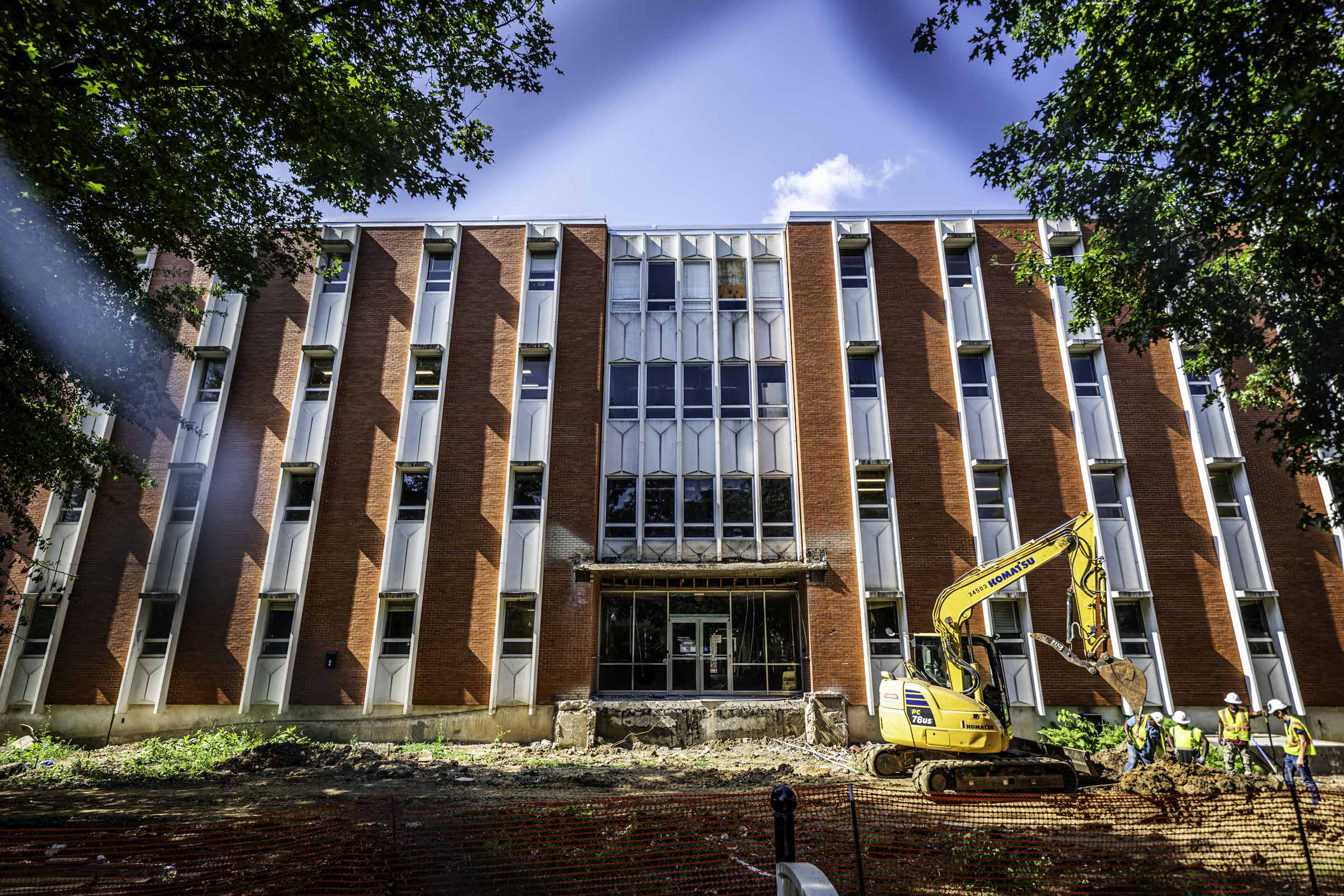 Exterior photos of Dorman Hall under construction, surrounded by dirt and debris- shot through a fence under a bright blue morning sky.