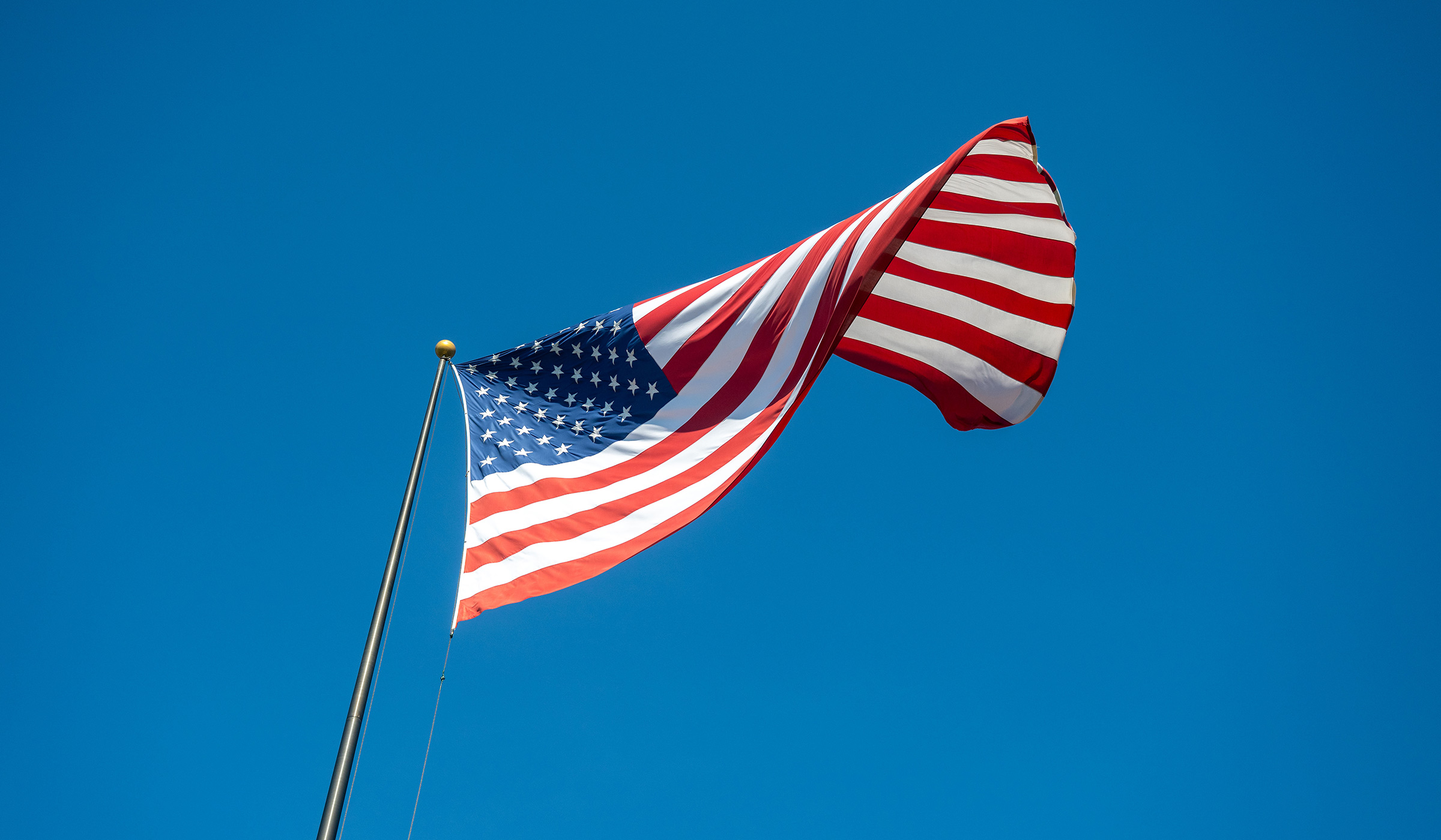 The American flag flies in a bright blue sky over the Drill Field.