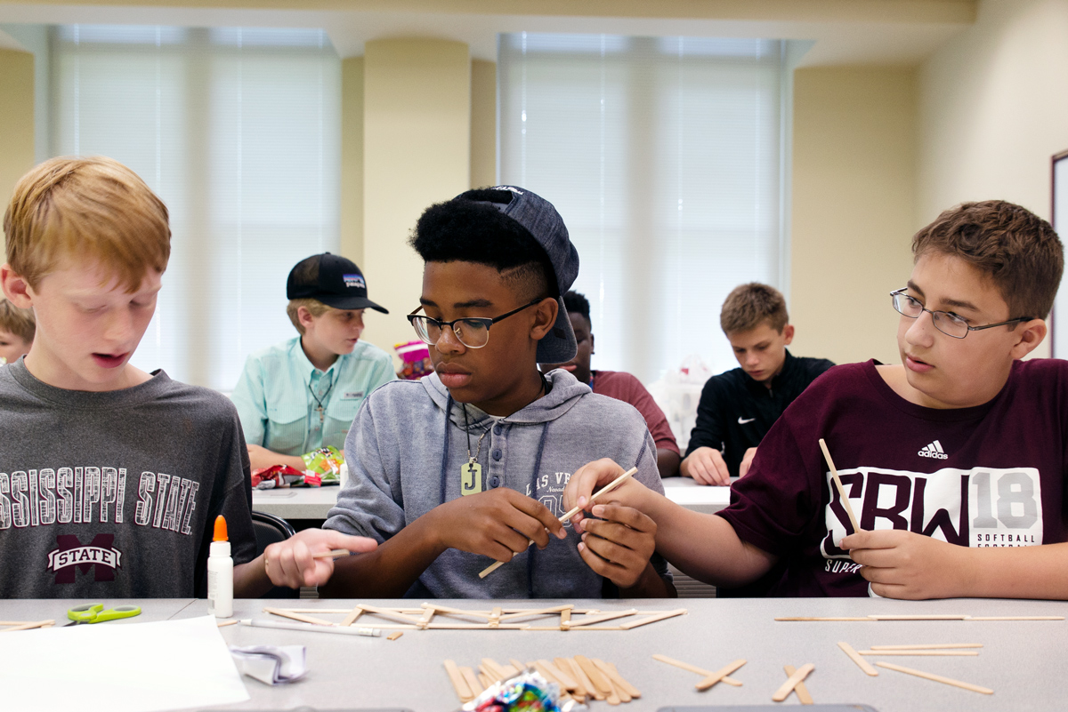 Three middle school students working together to create a Popsicle stick bridge