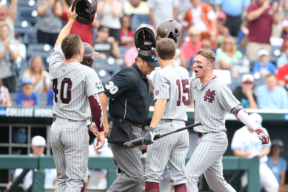 Baseball players in gray pinstripes knocking helmets together in celebration at home plate.