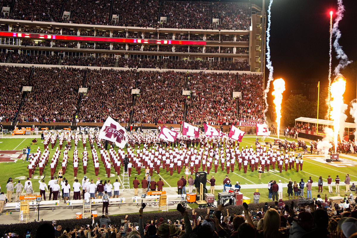 Cheerleaders running with flags that spell out state through marching band and pyrotechnics