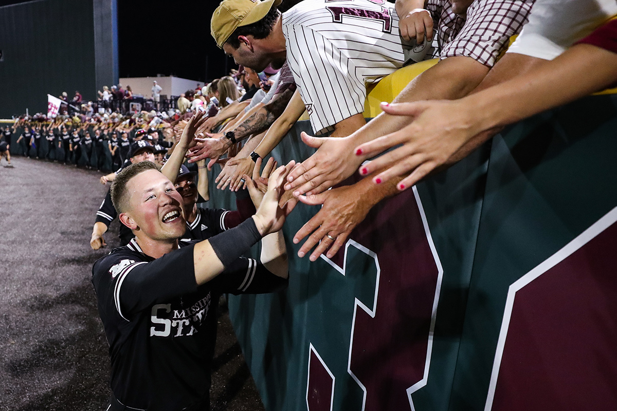 Guy in black MSU baseball uniform high fiving fans along outfield wall.