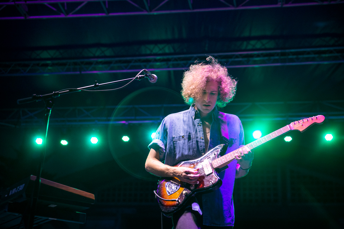 Guy with guitar on stage with green lights behind him.