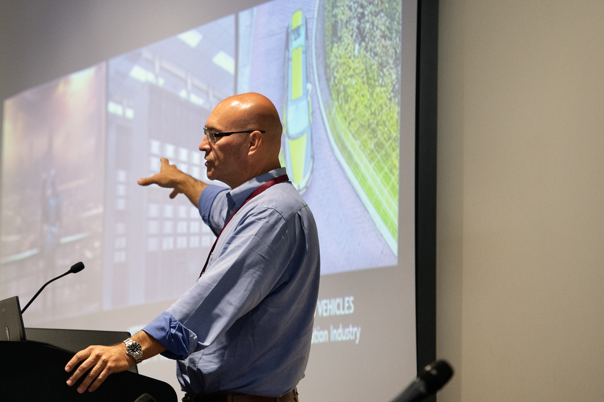 ROAD 2018 Keynote speaker Sanford Russell speas in front of projected images related to autonomous vehicles.