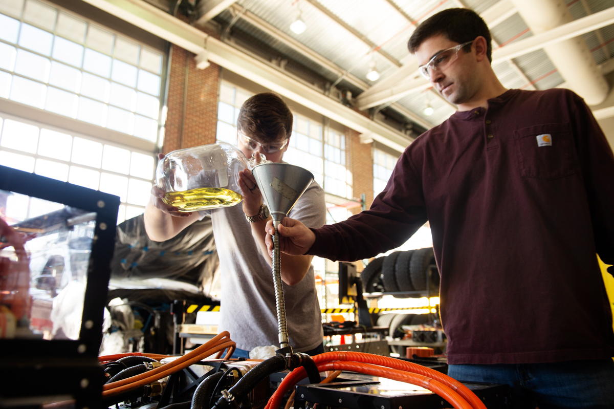 Graduate student Chad Leachman and Research Engineer Andrew LeClair concentrate on pouring dielectric collant via a funnel.