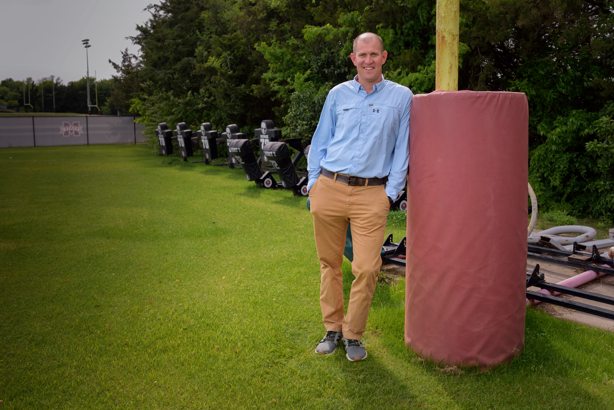 Michael Richard smiles for the camera while leaning up against a red and yellow goalpost.