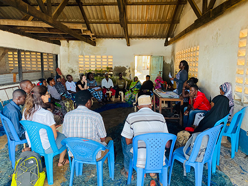 Several people sit and listen to a speaker as Fish Innovation Lab researchers meet with community members in coastal Kenya 