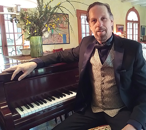 Bill Edwards, seated and with his right arm resting on a piano.