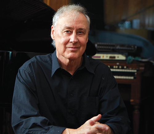 Portrait of musician Bruce Hornsby with a multi-keyed instrument in the background