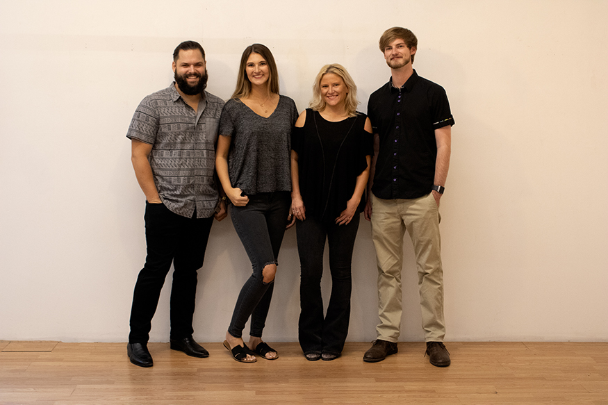 Group photo of four graduating MSU art/graphic design seniors standing in front of a wall