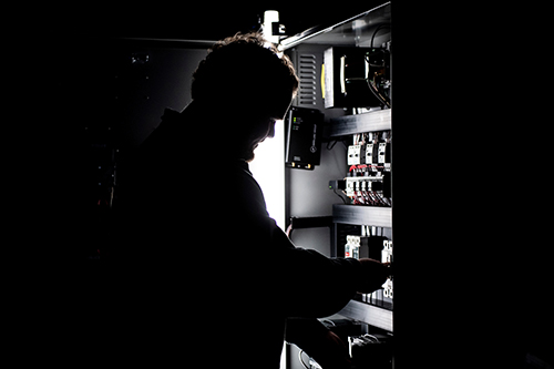 A man adjusts wires on a dimly lit computer server.