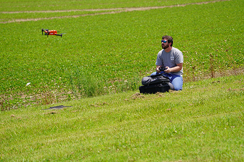 A man launches a drone in front of an agricultural field.