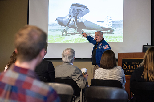 MSU students, administrators and guests look and listen as retired NASA astronaut Fred Gregory gestures to a photo of an airplane.
