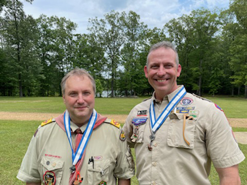 Gerhard Lehnerer, left, and Brent Fountain, right, are pictured wearing their Boy Scout volunteer shirts and smiling for the camera while standing in a grassy field.