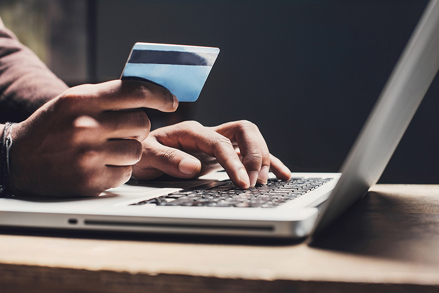 A close-up of a man's hands using a laptop computer while also holding a credit card