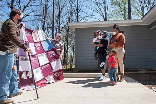 Retired U.S. Army Captain Matt Savage and Starkville resident Dot Livingston present a homemade MSU T-shirt quilt to 12th Maroon Edition homeowners Chadrick Robinson, Santana Turnipseed and two of their children