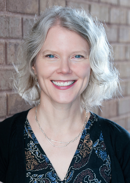 Becky Hagenston smiles while standing in front of a brick wall.