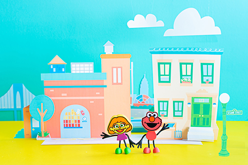 Elmo and Julia characters stand against a Sesame Street backdrop.