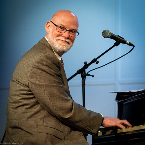 Jeff Barnhart turns toward the camera while seated at a piano.