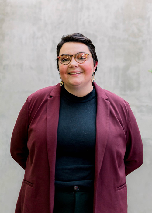 Rebecca Van Pamel smiles while standing in front of a white wall.