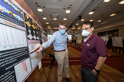 A student uses a maroon pen to point at his research poster while explaining the project to a judge during Mississippi State’s Summer Undergraduate Research Symposium.