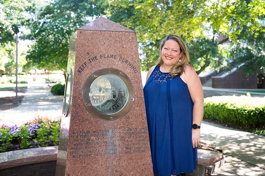 woman standing in front of allen hall eternal flame