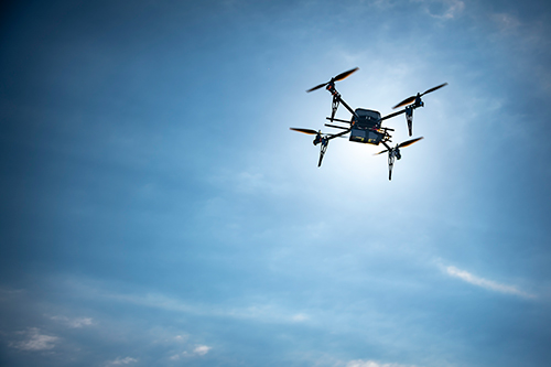 A UAV is shown in flight to the right side of the photo with a bright sunny sky filling the background