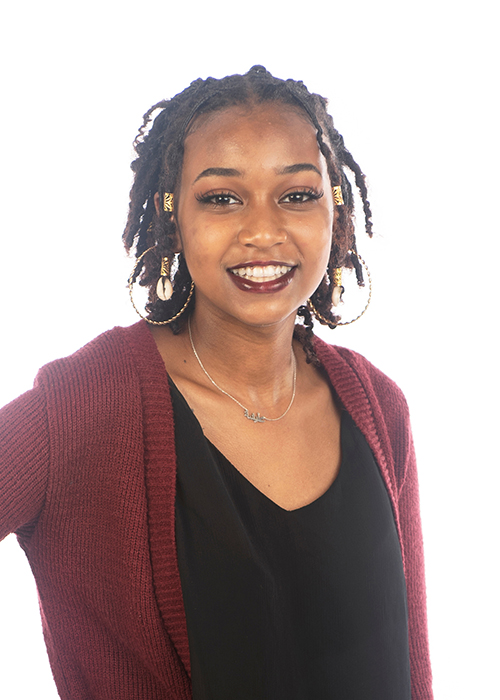 Alysia Williams smiles while standing in front of a white backdrop in a photo studio.
