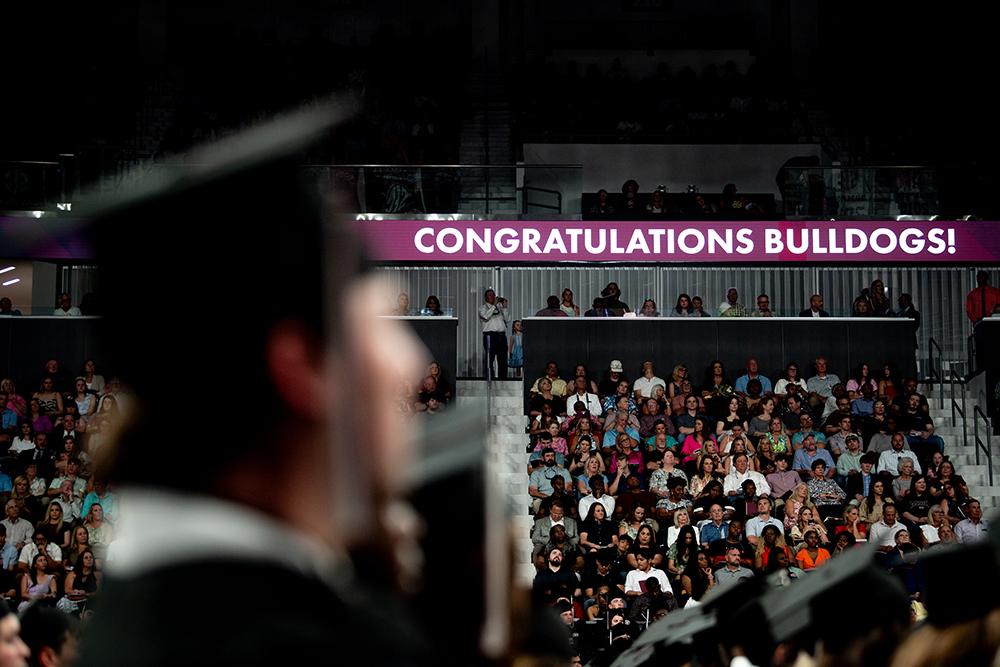 A banner reading "Congratulations, Bulldogs!" is displayed during commencement at Humphrey Coliseum.