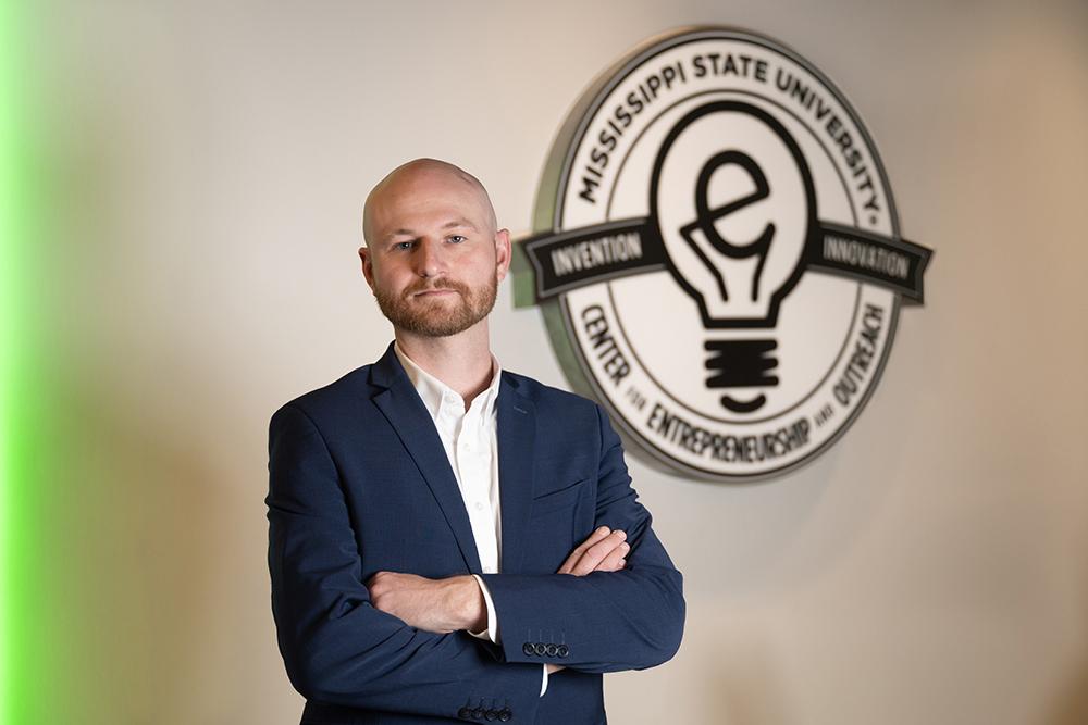 Nick Pashos poses in the McCool Hall E-Center, next to the center&#039;s wall-mounted logo.
