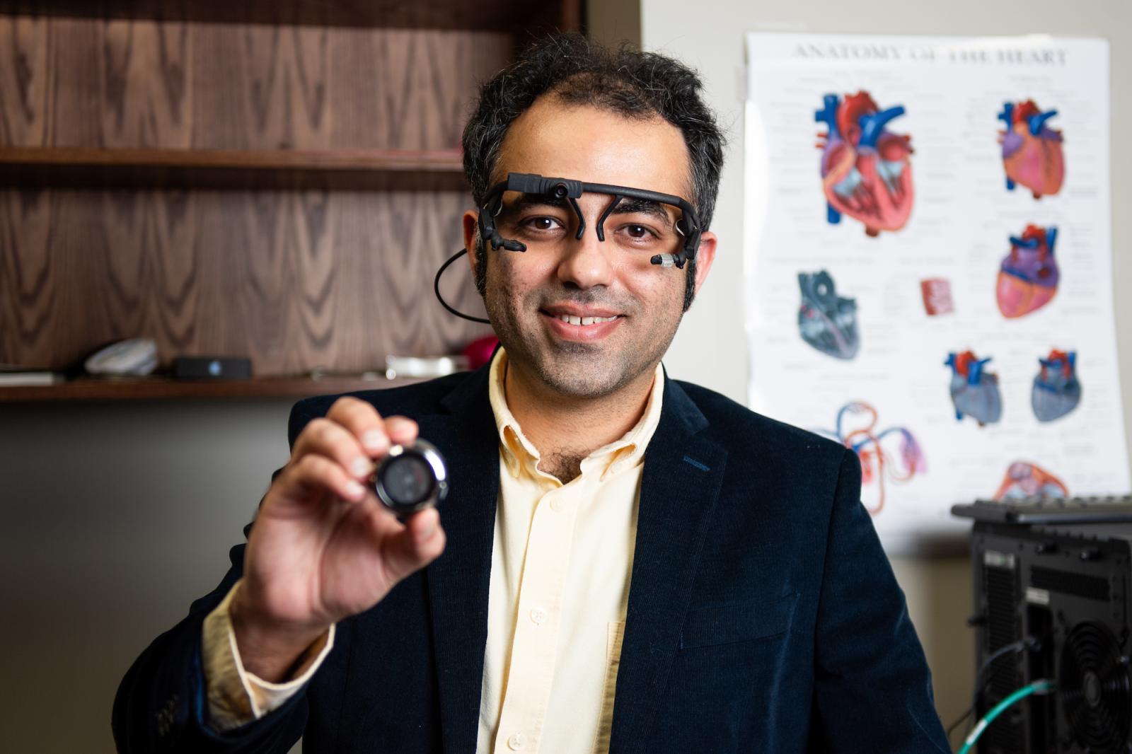 Amirtahà Taebi, assistant professor of biomedical engineering, wears an eye-tracking headset and holds an electronic stethoscope, both used to help develop new products and test methods in Taebi Lab. (Photo by Grace Cockrell)