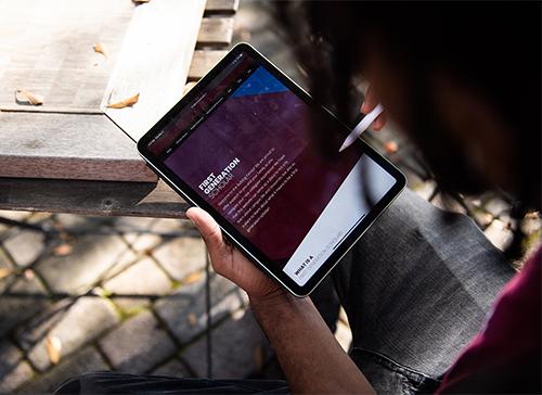 A first-generation student looks at a tablet and the MSU First Generation Scholar website