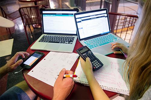 Students work with calculators and laptop computers.