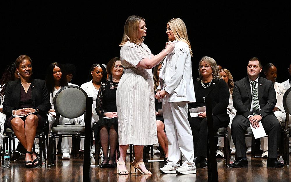 Kayla Carr, Mississippi State University-Meridian professor of nursing, pins graduate Olivia Adams of Philadelphia at Thursday's [Aug. 7] inaugural Master of Science in Nursing pinning and graduation ceremony.