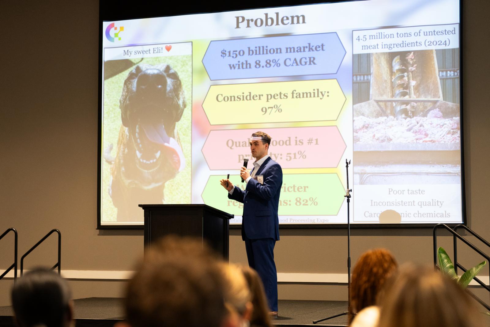 young man in suit speaking to crowd in front of screen