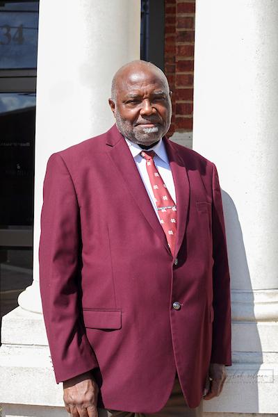 man in maroon blazer in front of white columns